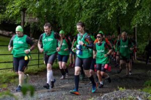 A mixed team of runners in wetsuits and Great SwimRun tabards run along a stony path looking focused and determined