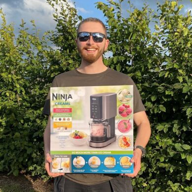 Man wearing sunglasses smiling at the camera holding a boxed ice cream maker
