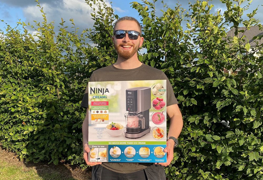 Man wearing sunglasses smiling at the camera holding a boxed ice cream maker