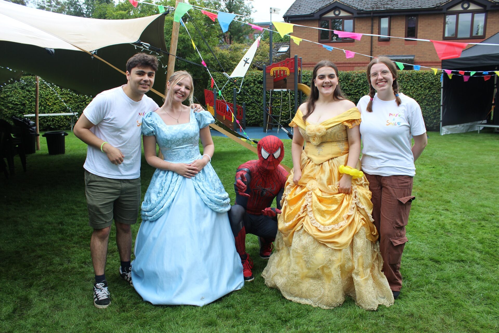 People dressed in princess and spiderman costumes stood on a lawn in front of a tent with colourful bunting hanging from it