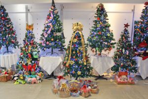 Rows of Christmas trees decorated with lights, baubles and gifts in a shop lined up against a white wall