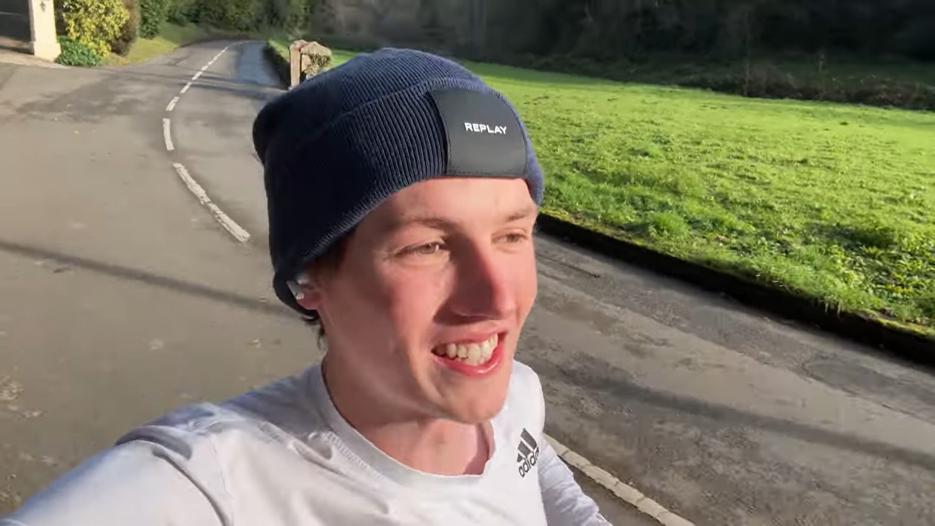 Man wearing a white top and black running hat as he runs along a road smiling