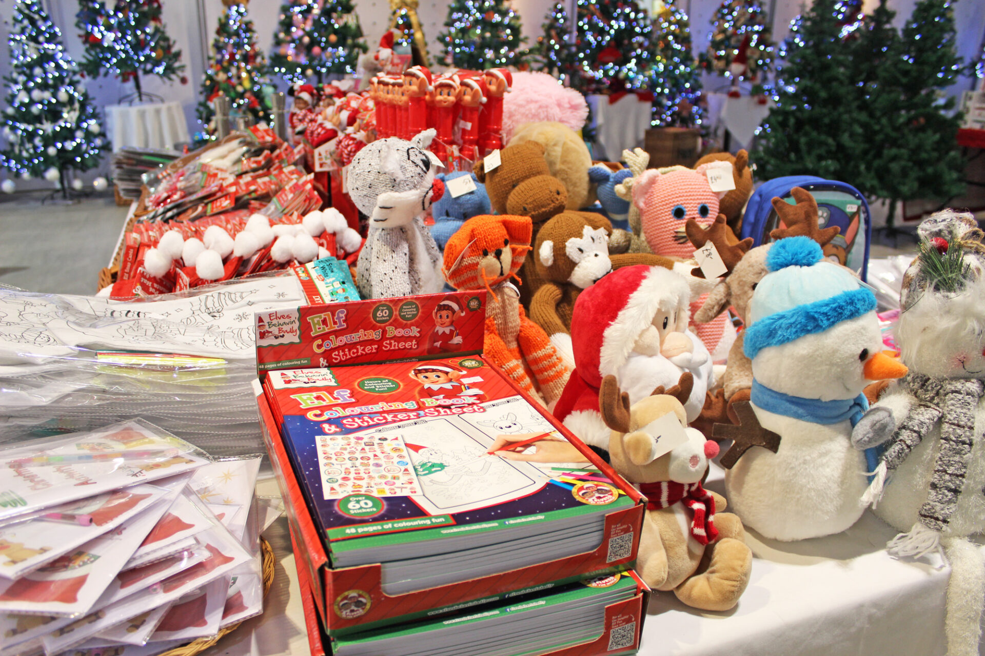 Christmas soft toys and books on a table in a shop displaying Christmas trees