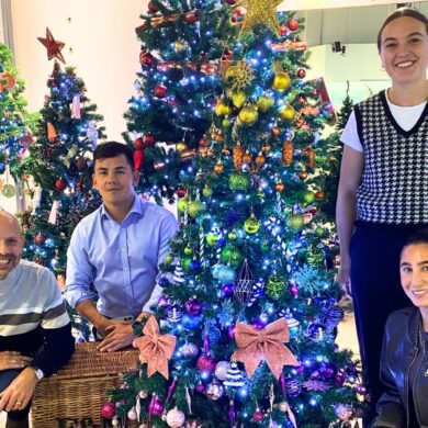 Four people stood and kneeling next to a decorated Christmas tree