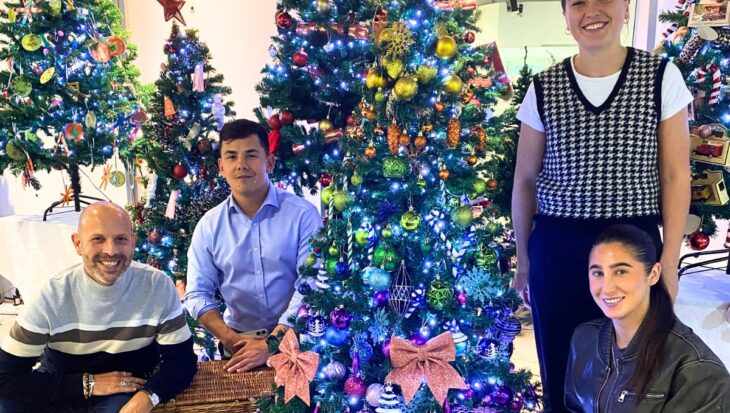 Four people stood and kneeling next to a decorated Christmas tree