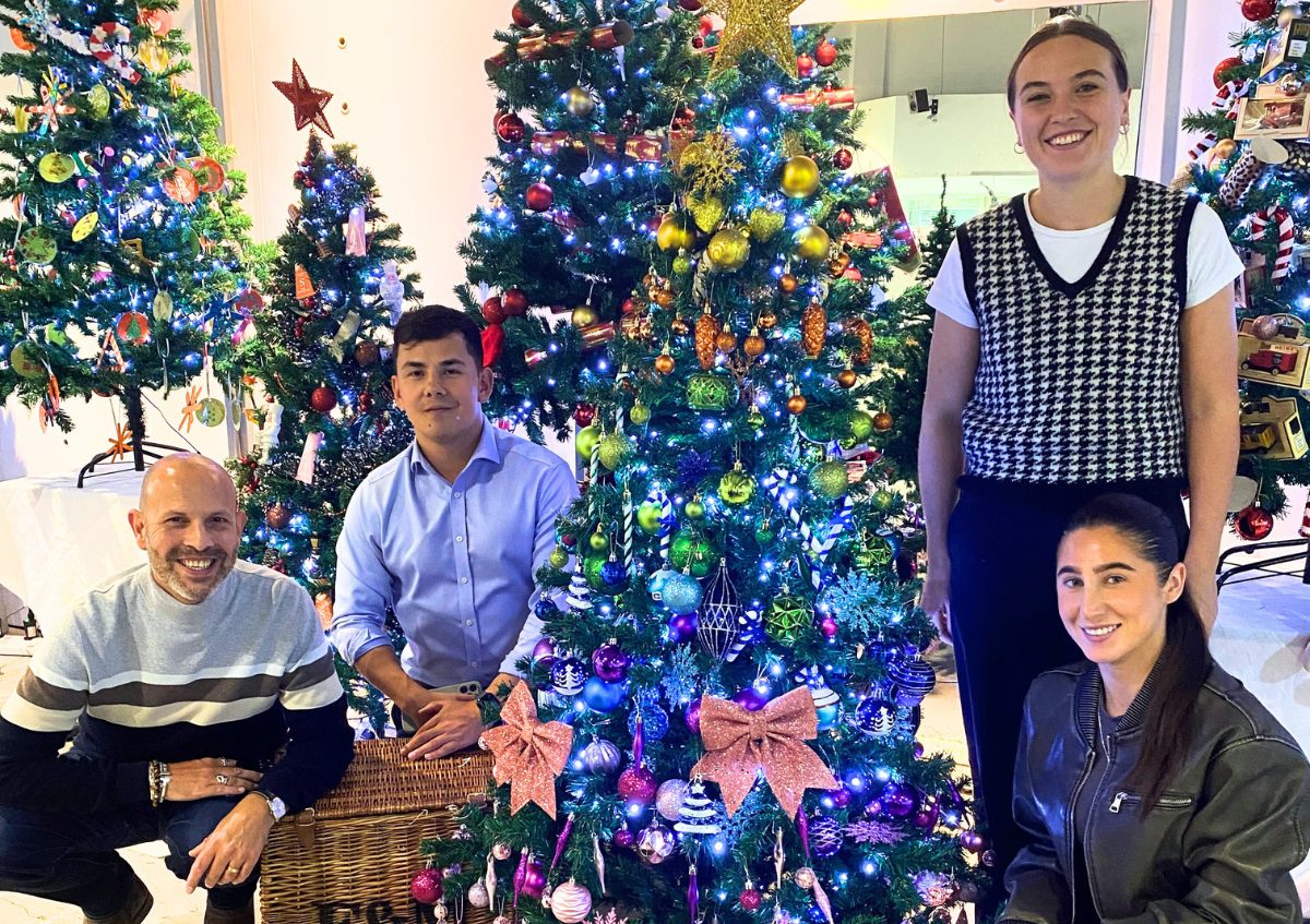 Four people stood and kneeling next to a decorated Christmas tree