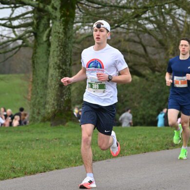Man wearing white running t-shirt and cap running in a park with other people