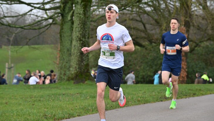 Man wearing white running t-shirt and cap running in a park with other people