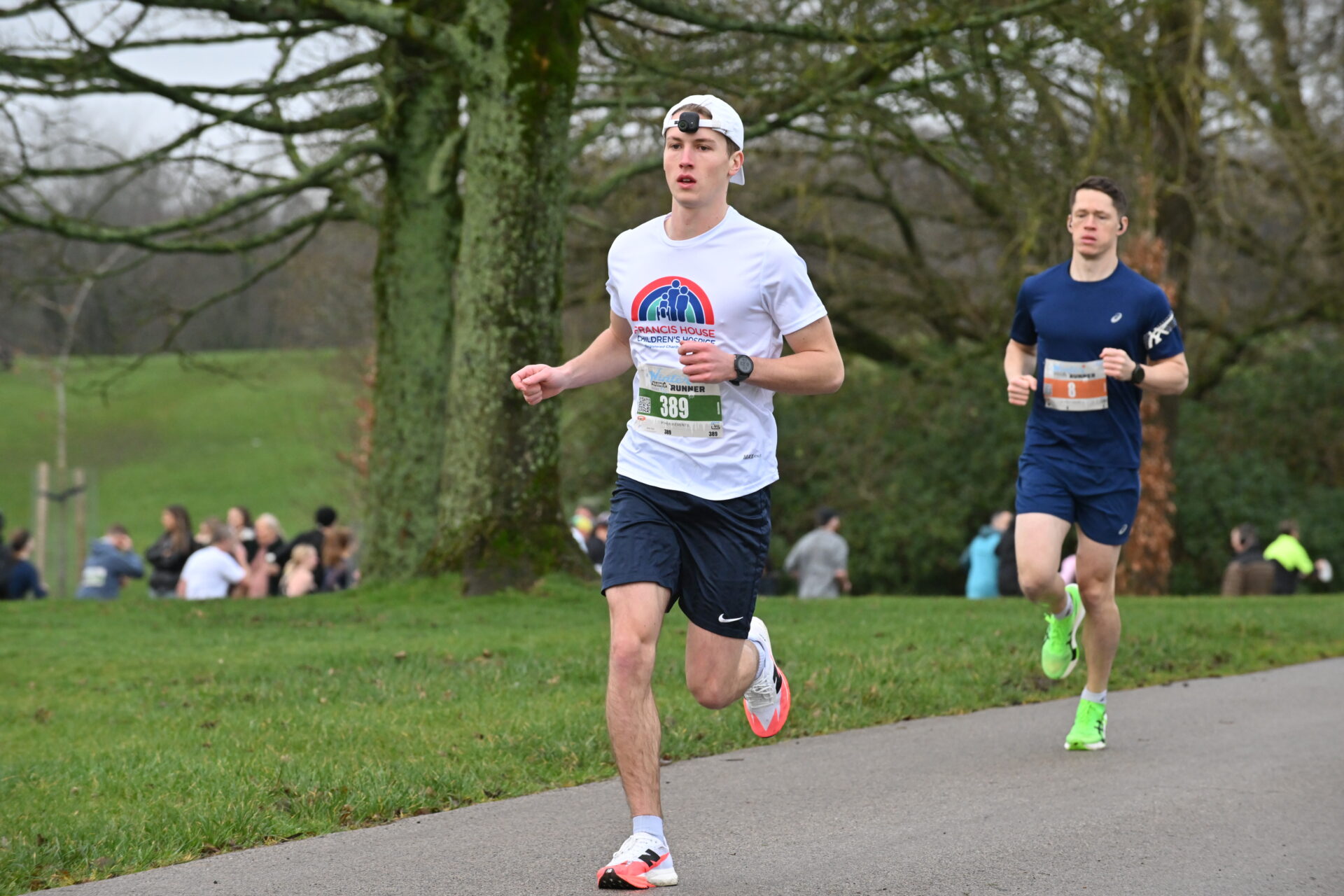 Man wearing white running t-shirt and cap running in a park with other people