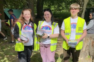 Three people wearing hi-vis vest holding leaflets volunteering at Bramhall duck race.