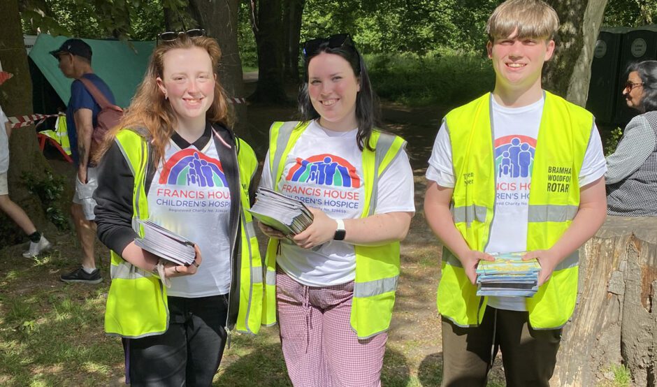 Three people wearing hi-vis vest holding leaflets volunteering at Bramhall duck race.