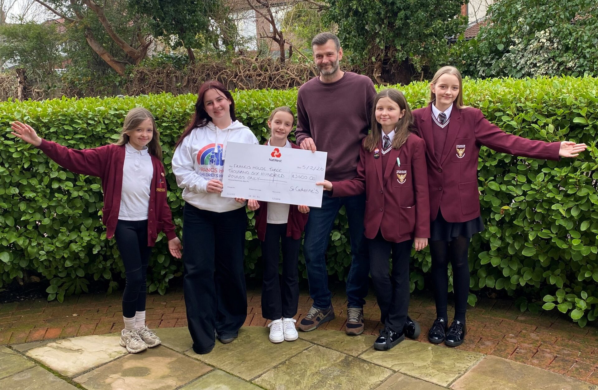 A man and a woman stood with a group of school children holding a large cheque and smiling at the camera