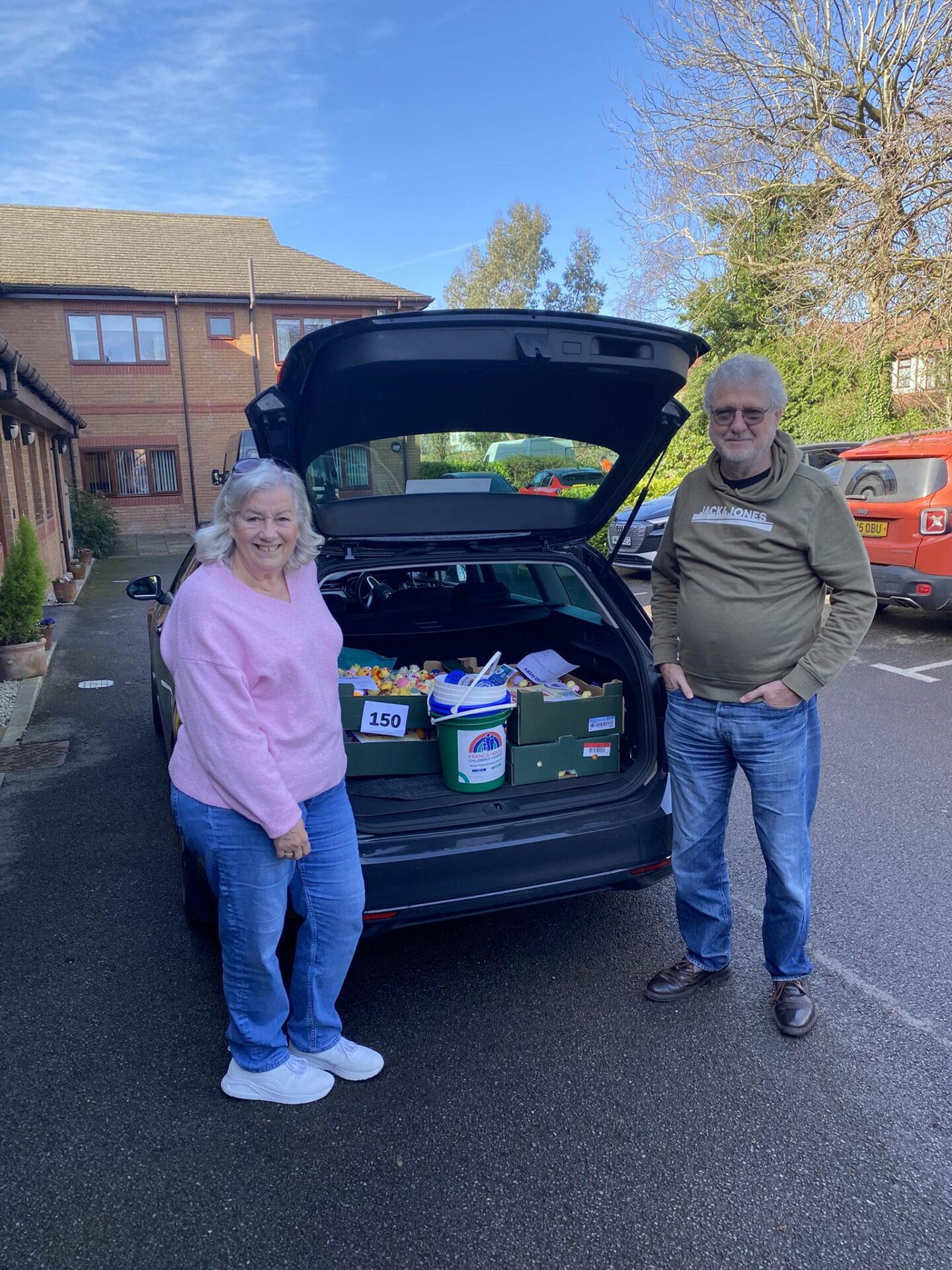 A woman and a man stand beside an open car boot loaded with crates of Easter Chicks and fundraising buckets