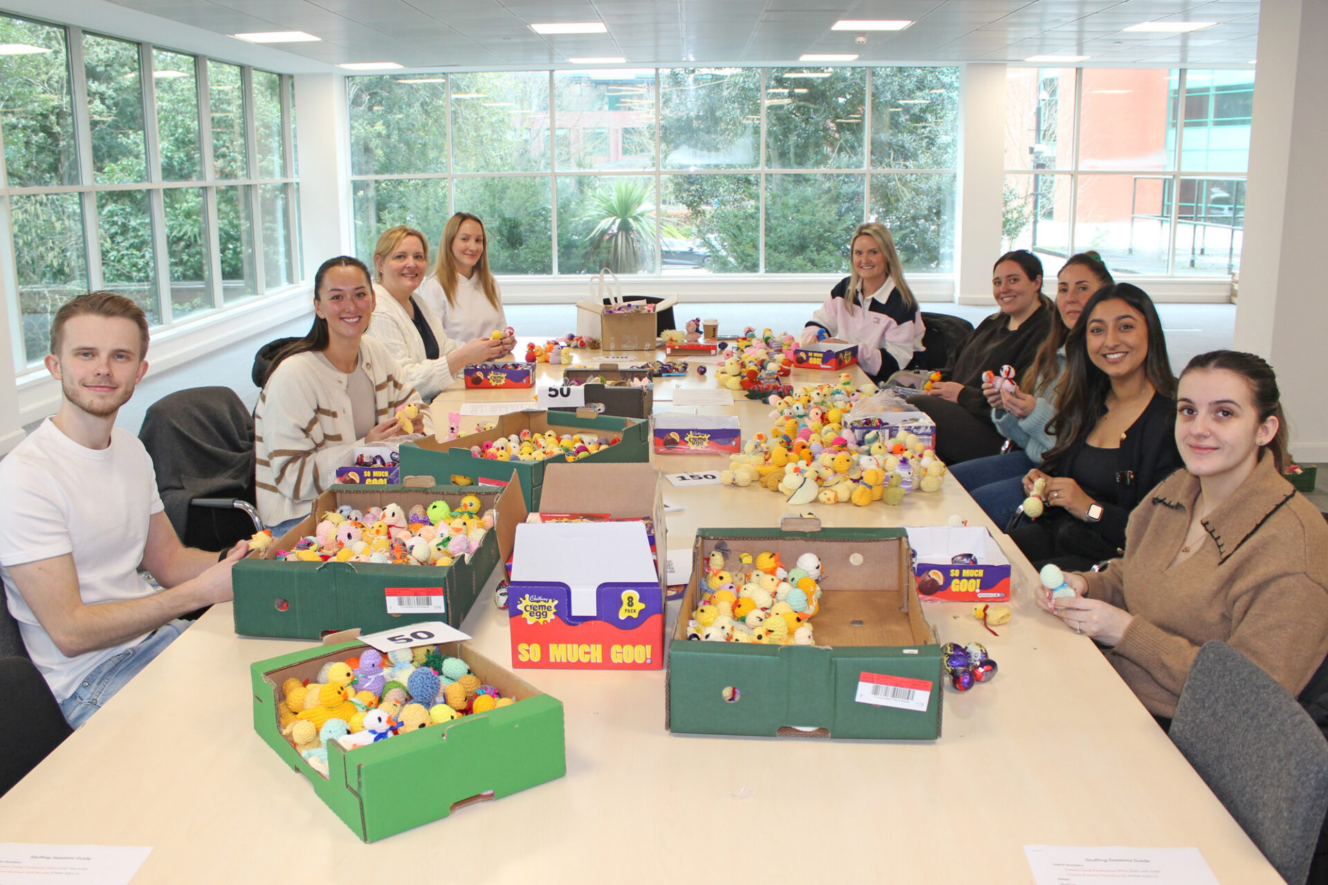Volunteers sit around a big table full of boxes of chicks and chocolate eggs