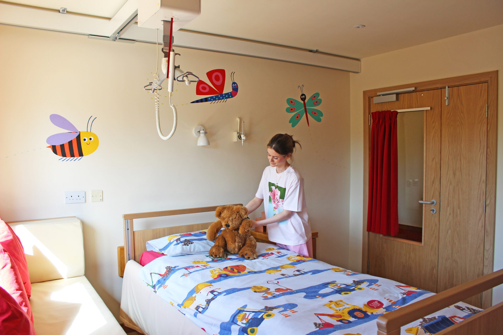 Young woman placing a teddy bear on a child's bed in a colourful bedroom with painted bug cartoons in the walls