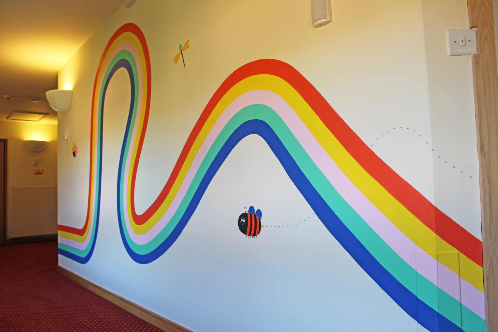 rainbow mural painted along a wall in a corridor