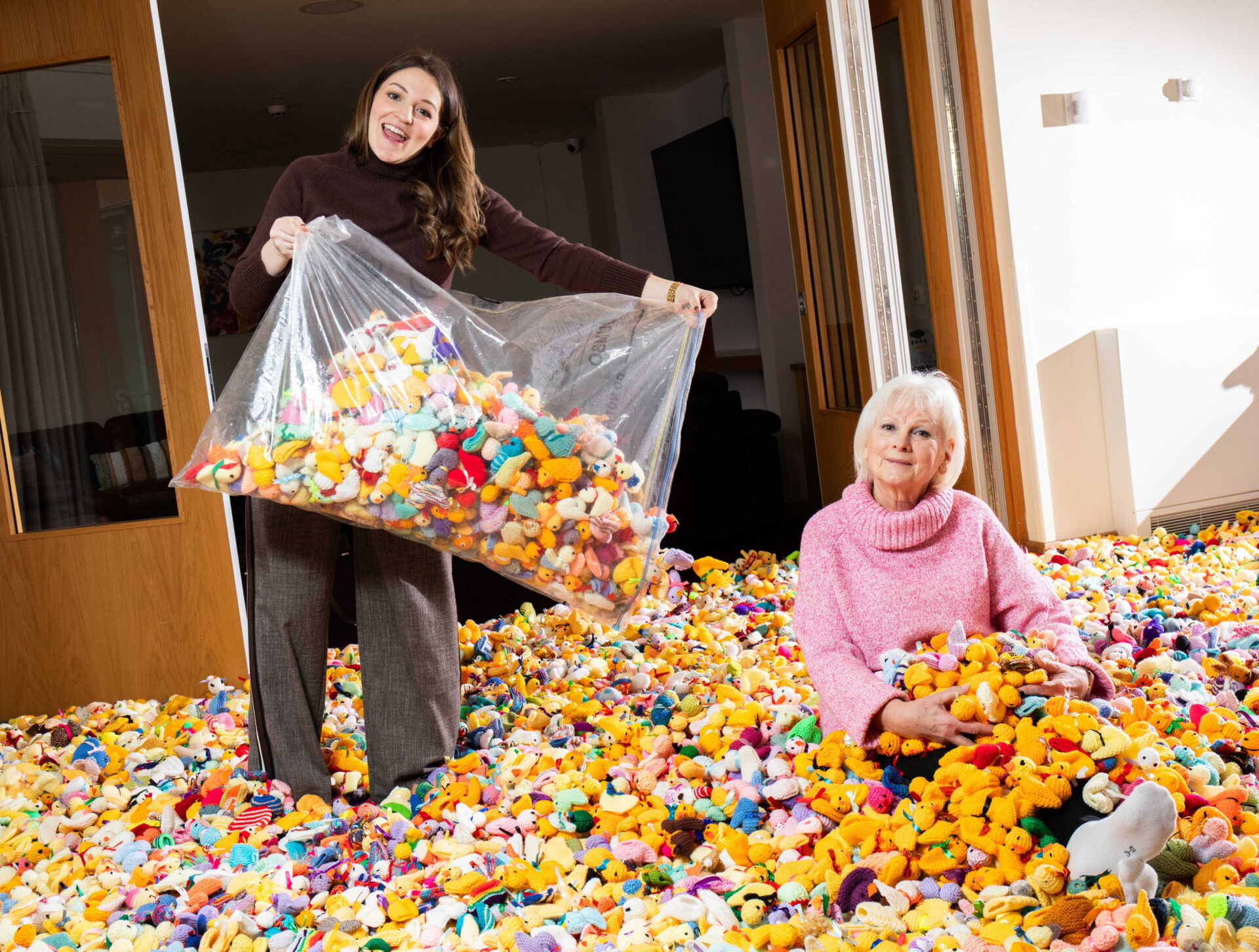 Rachel Nasiri tips a large bag of knitted chicks on the floor next to Maria Dunbobbin sat surrounded by knitted chicks and bunnies