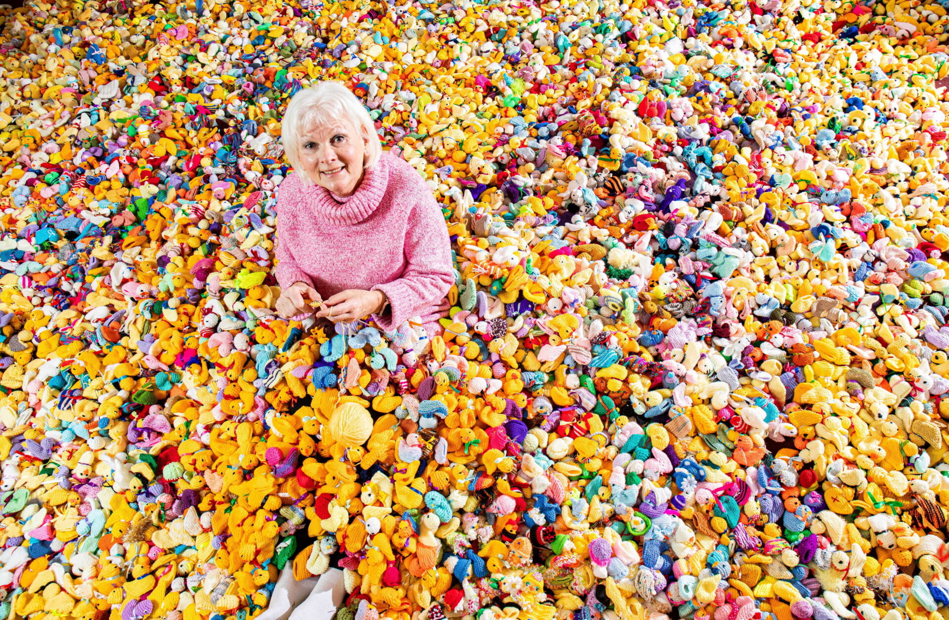 Woman Maria Dunbobbin sat in a pile of thousands of colourful knitted chicks