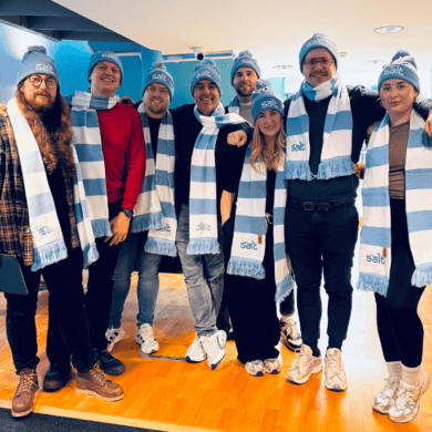 Group of people wearing blue and white striped scarves and hats stood in an office setting