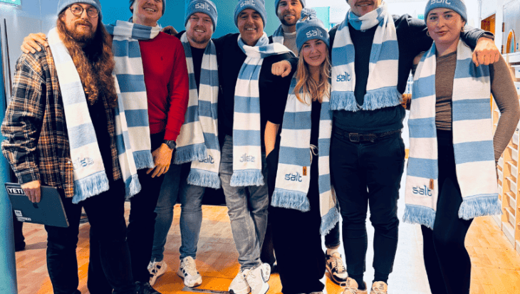 Group of people wearing blue and white striped scarves and hats stood in an office setting