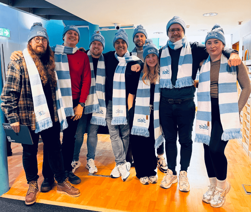 Group of people wearing blue and white striped scarves and hats stood in an office setting