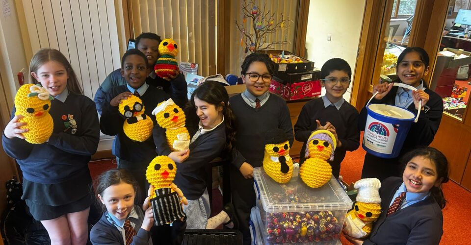 Children in school uniform pose with giant knitted chicks amongst boxes full of Creme Eggs