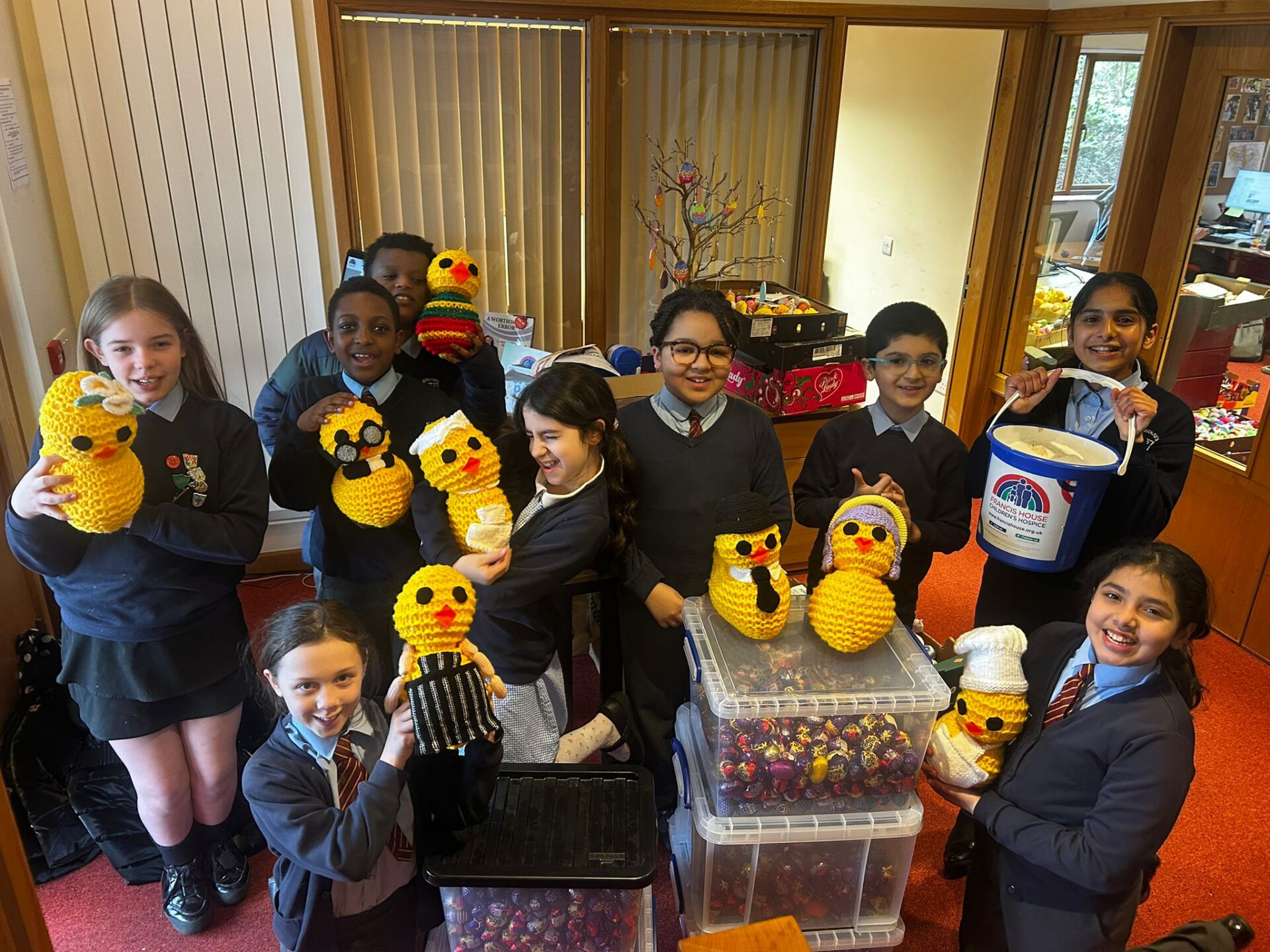 Children in school uniform pose with giant knitted chicks amongst boxes full of Creme Eggs