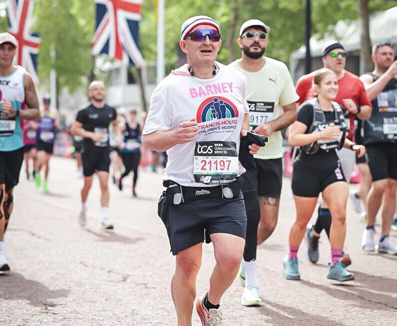 Group of people running the London Marathon with union jack flags in the background.