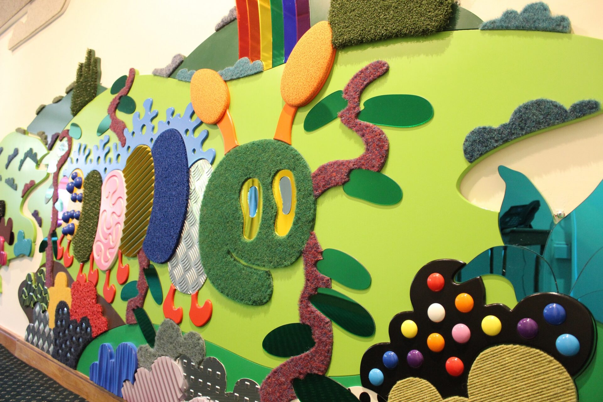 Wall covering made up of textured and coloured materials in the shape of a caterpillar
