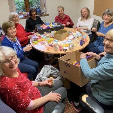 Group of women sat around a small table filling knitted chicks with chocolate eggs