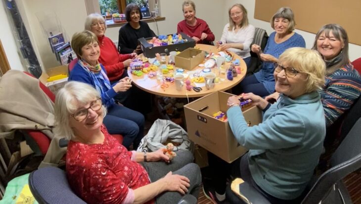 Group of women sat around a small table filling knitted chicks with chocolate eggs