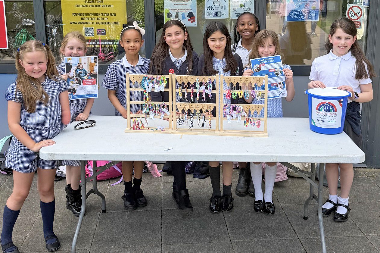 Group of school children selling bracelets hanging on stands from a table outside a shop