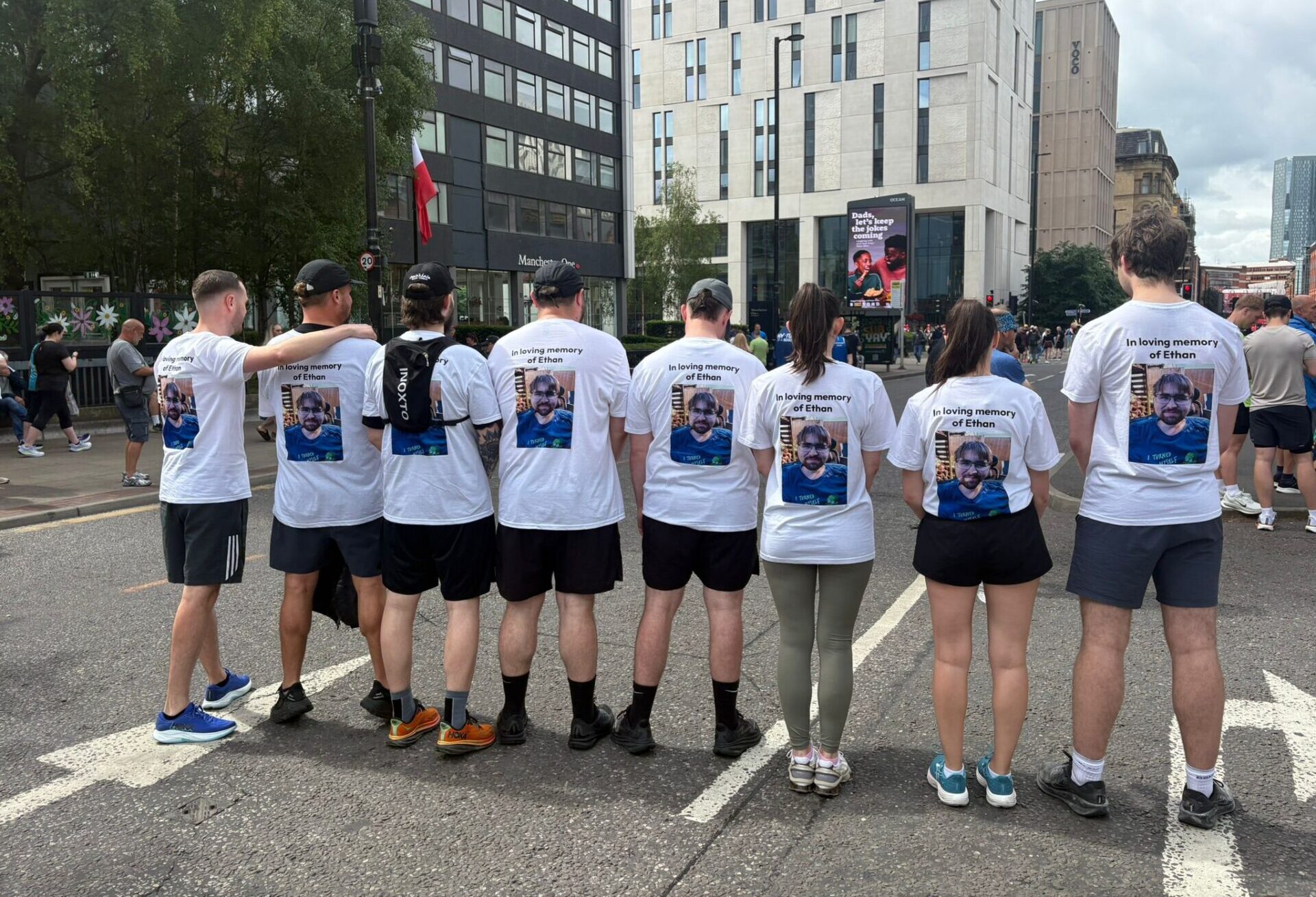 Group of eight runners wearing white t-shirts with a photo in loving memory of Ethan. They have their backs to the camera and are stood on a road.