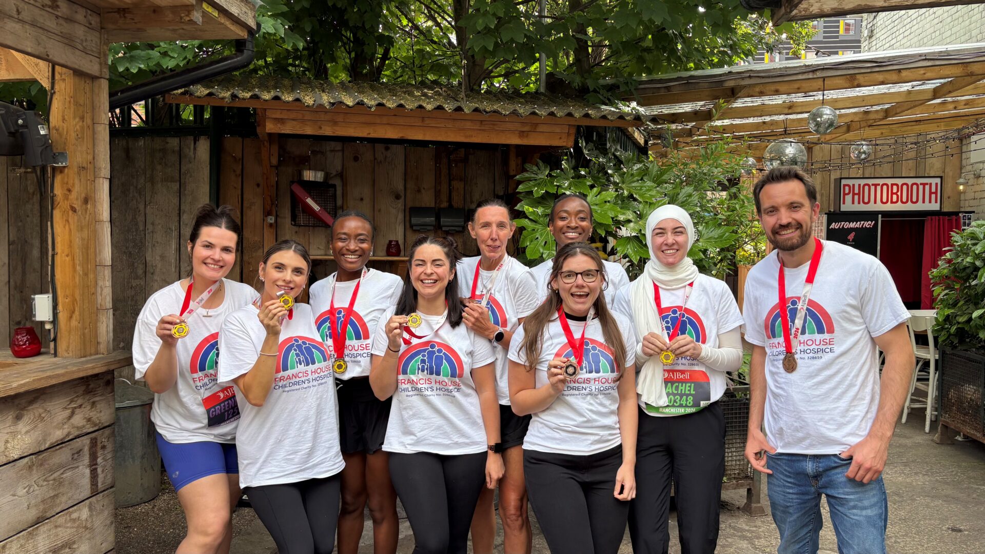 Group of eight women and one man wearing white t-shirts with a rainbow coloured logo, they hold medals and are smiling at the camera
