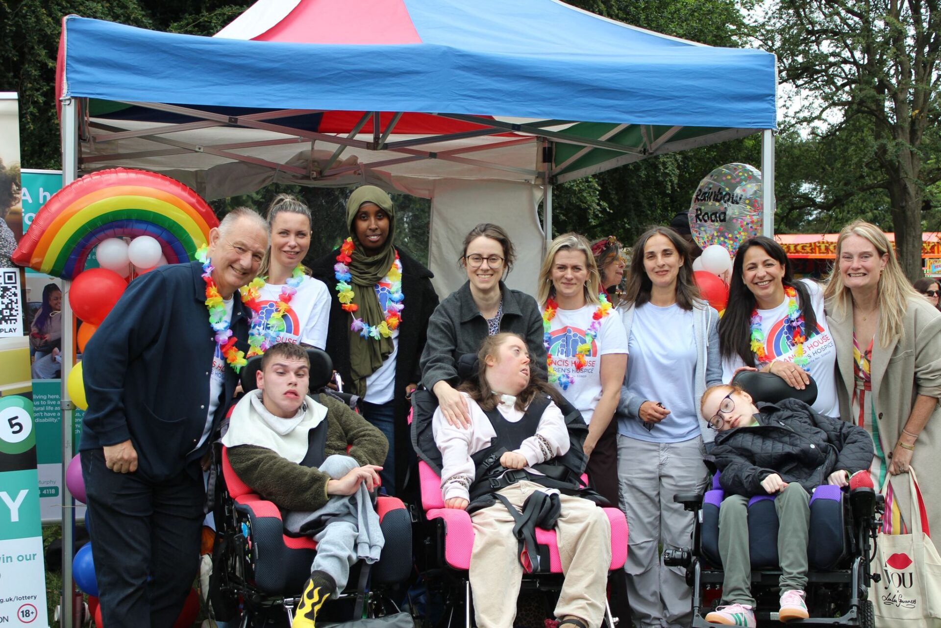 Group of adults and young people in wheelchairs sat by a colourful gazebo smiling at the camera