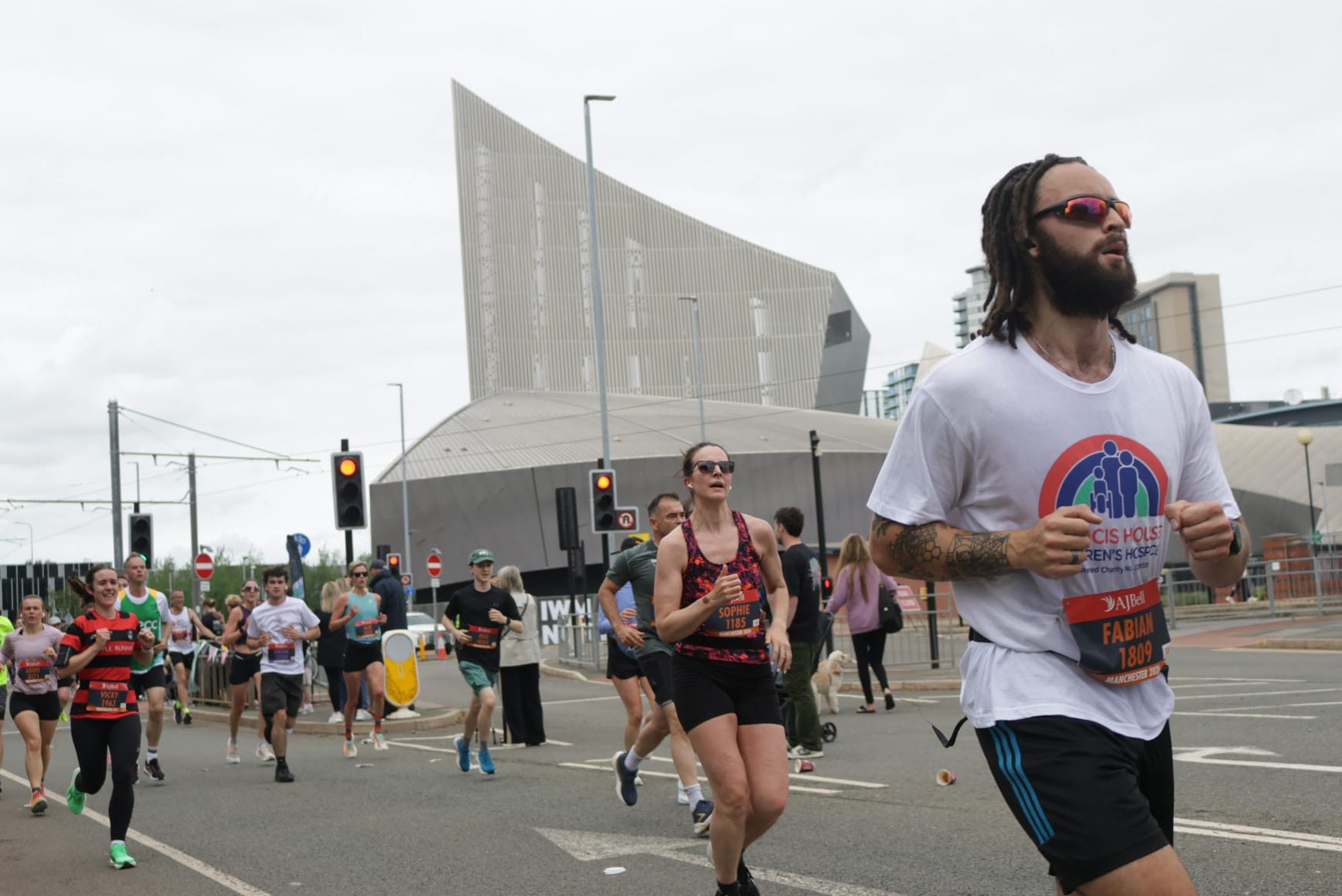 Group of runners led by a man wearing sunglasses running down a city street