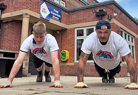 Two men doing push ups outside a pub, they are wearing white t-shirts with a rainbow coloured logo