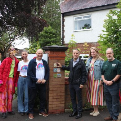 Group of men and women stood next to a wall which has painted ceramic tiles on it