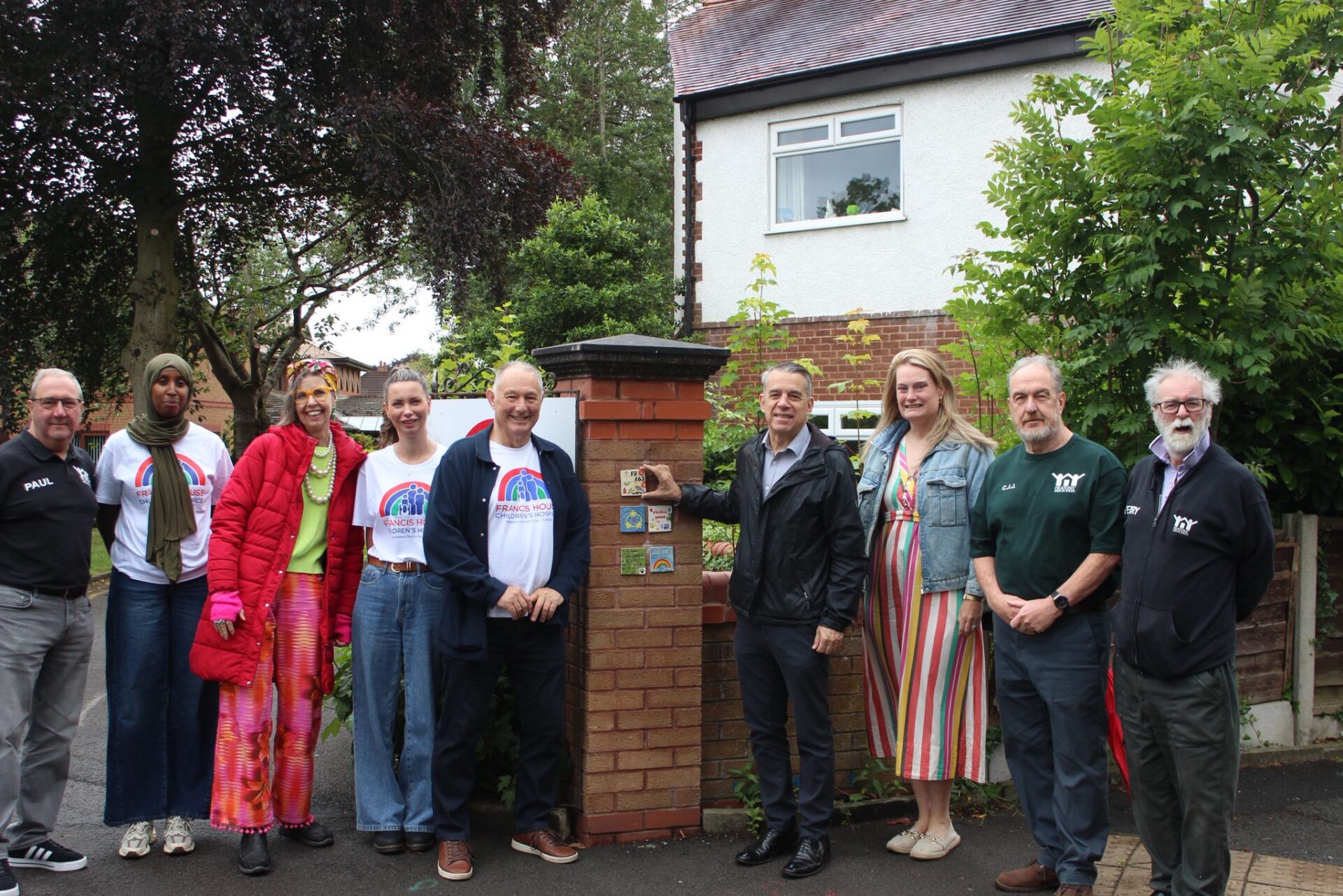 Group of men and women stood next to a wall which has painted ceramic tiles on it