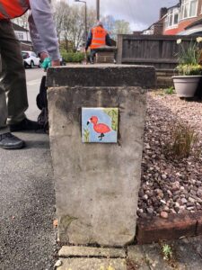 A concrete fence post in a suburban street with a ceramic tile painted with a flamingo on it