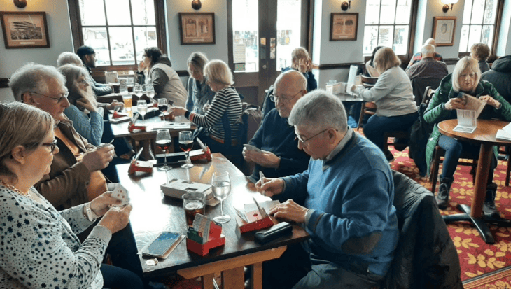 People seated in a cafe around tables playing the card game bridge
