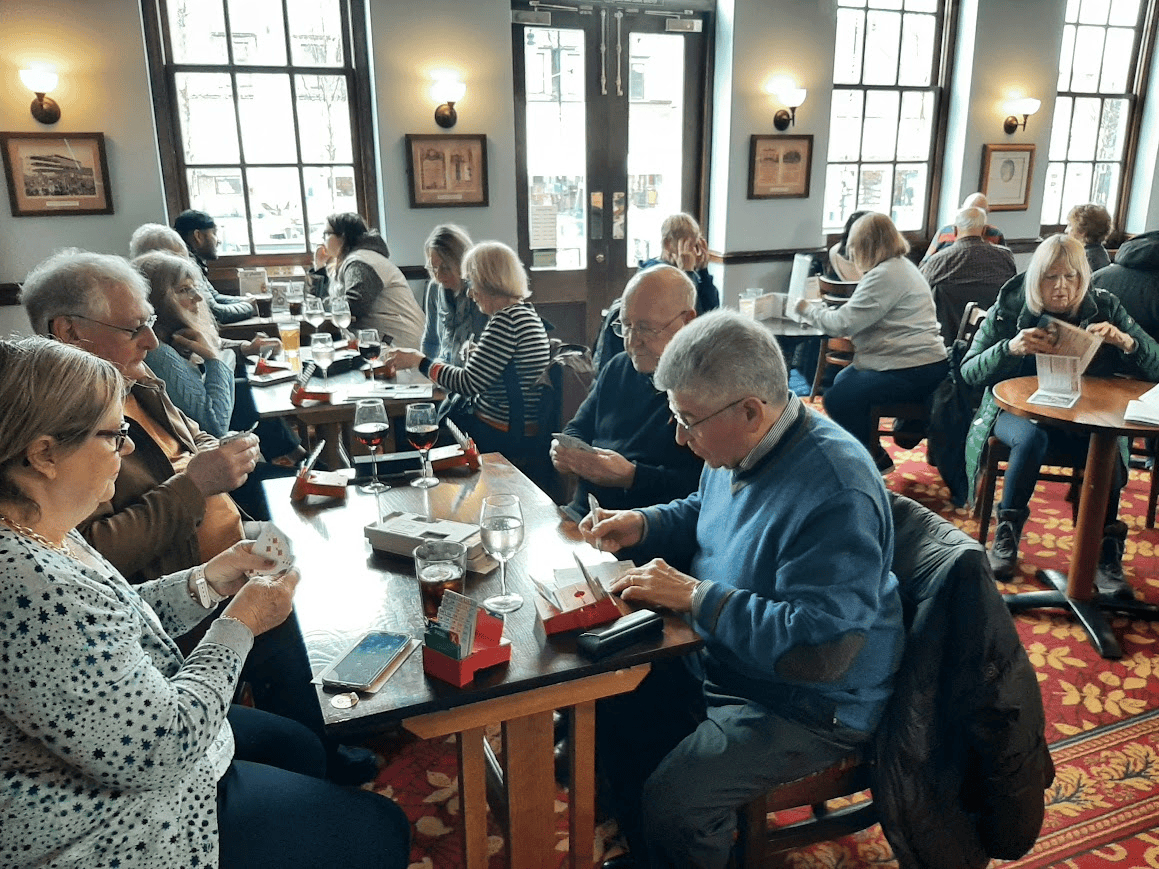People seated in a cafe around tables playing the card game bridge