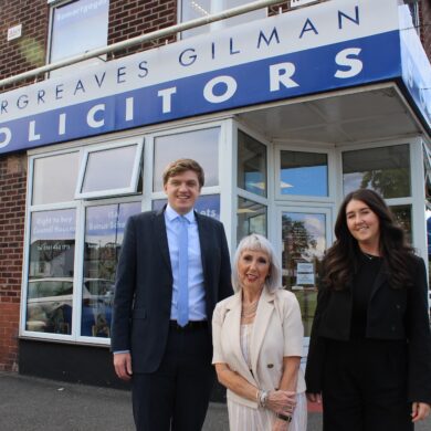 A man and two women smartly dressed stood outside a solicitors office with a sign saying Hargreaves Gilman Solicitors