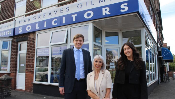 A man and two women smartly dressed stood outside a solicitors office with a sign saying Hargreaves Gilman Solicitors