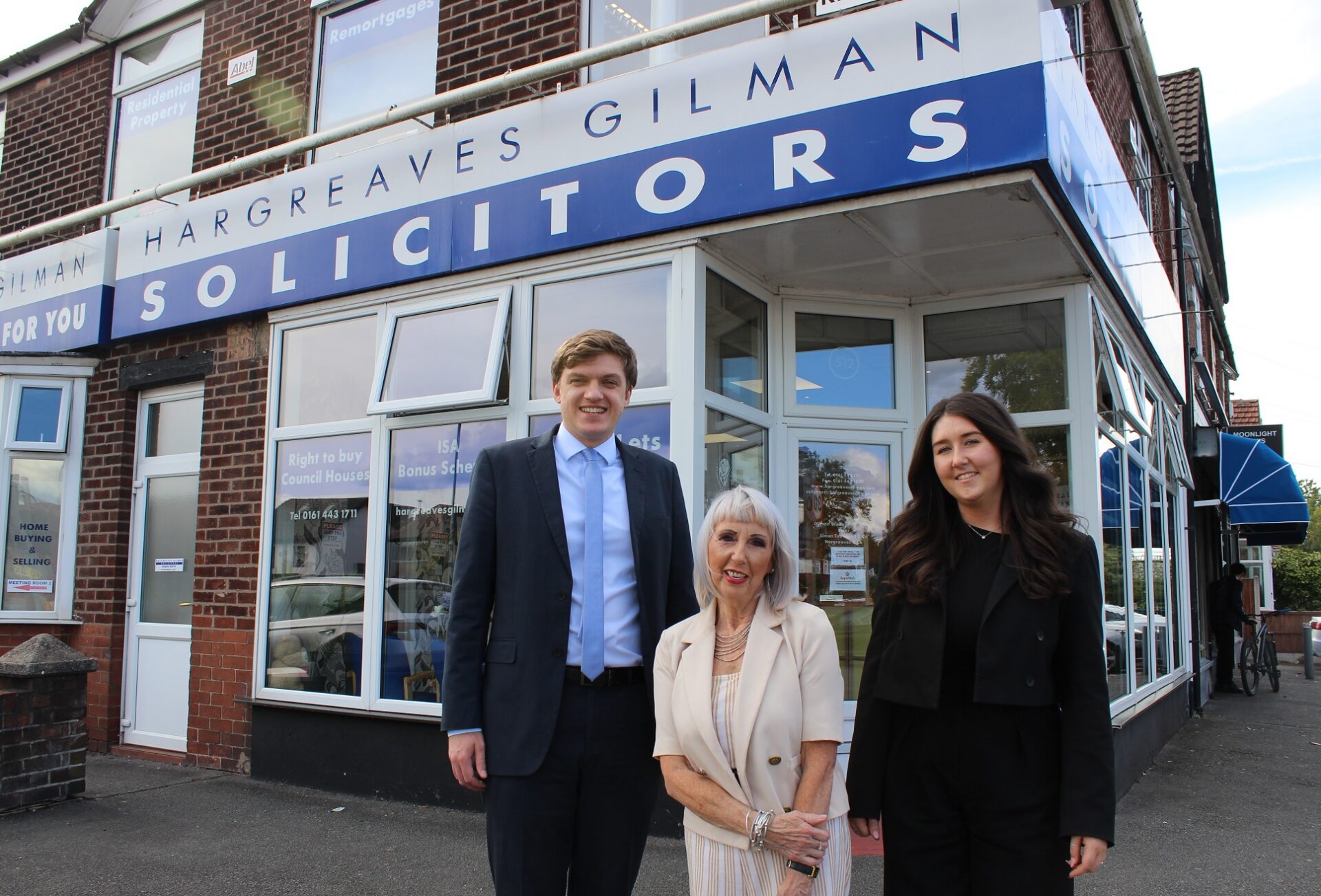 A man and two women smartly dressed stood outside a solicitors office with a sign saying Hargreaves Gilman Solicitors