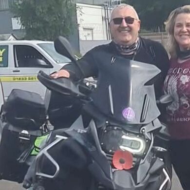 Man and woman stood next to a motorbike in a car park smiling at the camera