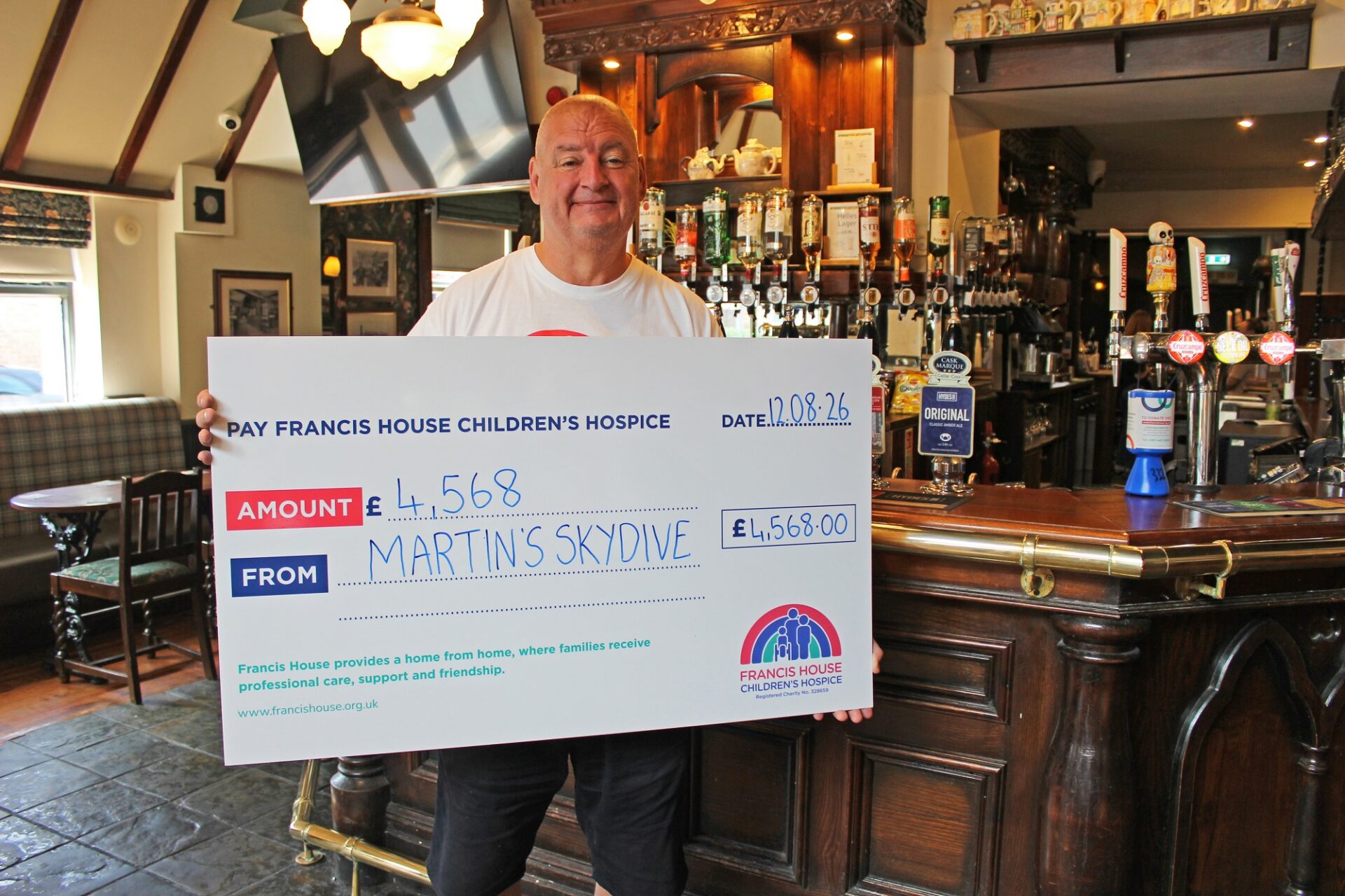 man stood in a pub by the bar holding a large cheque with the amount £4,568 for Martin's skydive written on it