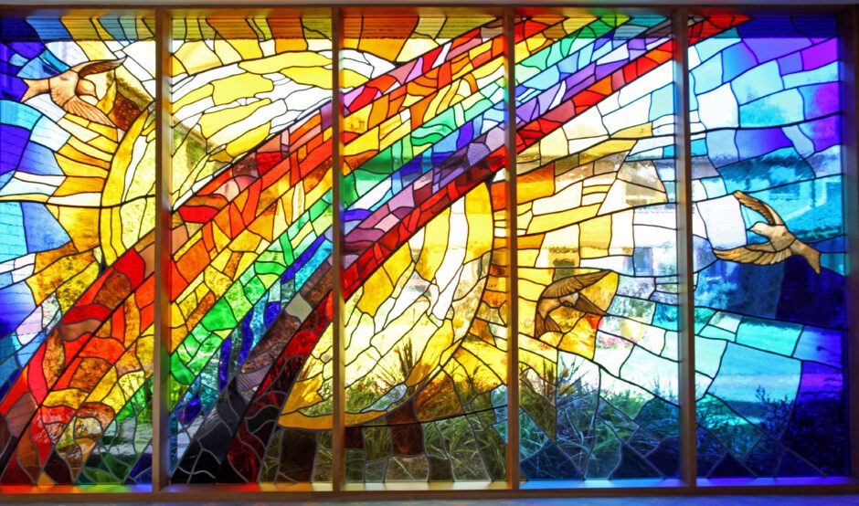 Stained glass window of a rainbow in front of a sun and doves flying