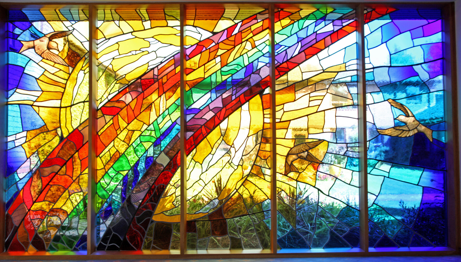 Stained glass window of a rainbow in front of a sun and doves flying
