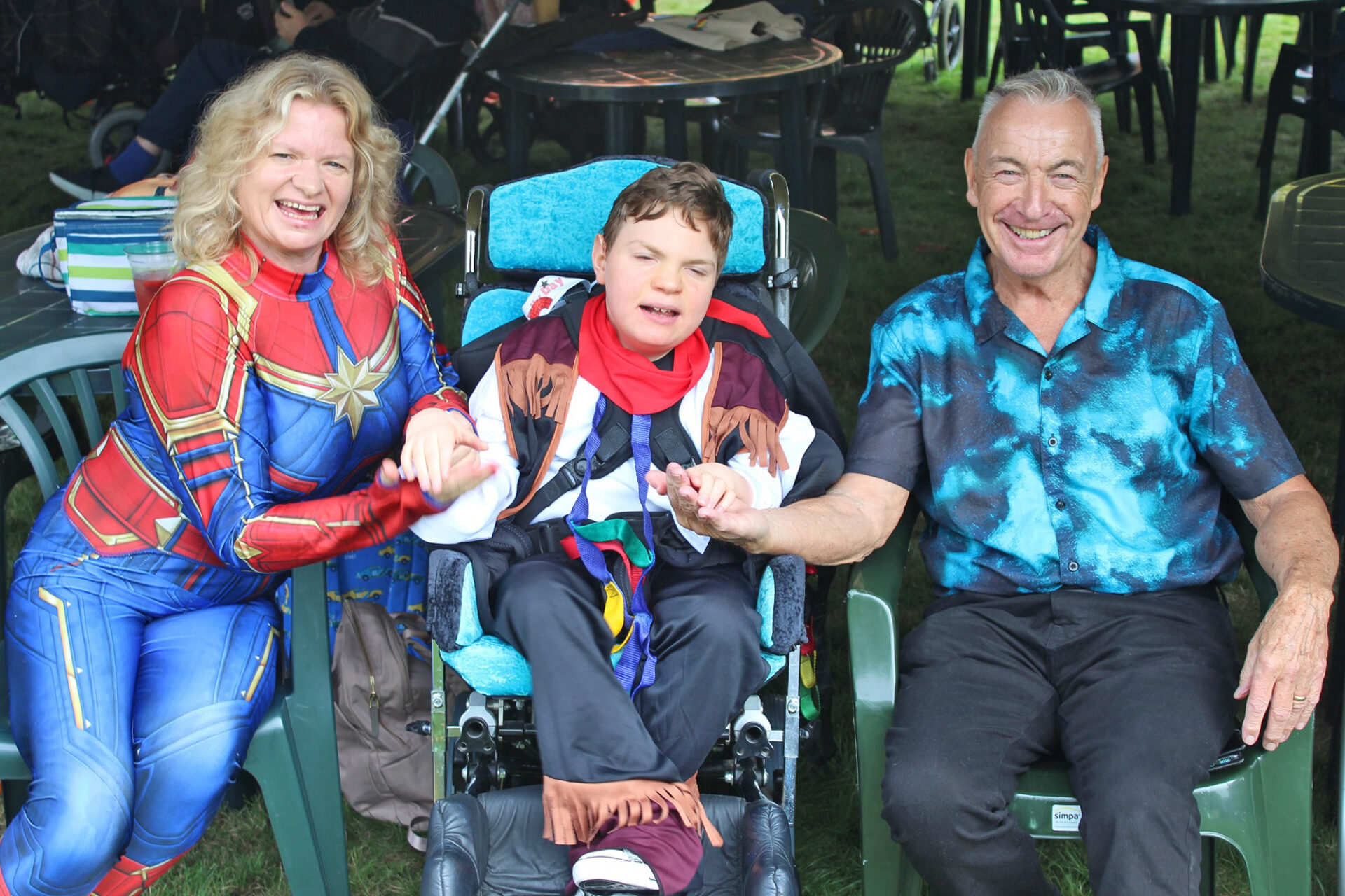 Woman wearing a superhero outfit sat with boy in a wheelchair and a man smiling at the camera